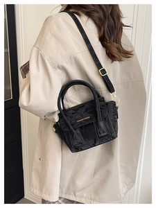 Detail of black textured crossbody bag with gold text and adjustable leather strap