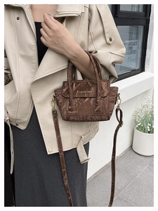 Brown pleated handbag with patent finish and dual handles shown on a female model