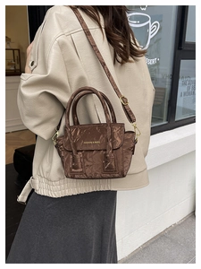 Detail of dark brown pleated texture crossbody bag with gold hardware on a street model