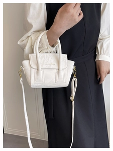 Detailed side view of white pleated leather handbag worn by model with gold hardware