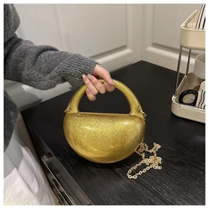 Close-up of sparkling gold evening bag with ring handle and metal chain strap