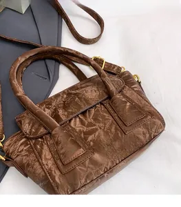 Detail of coffee brown pleated handbag with golden buckles and fashion text logo
