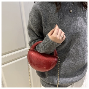 Detail of red glitter semi-circle evening bag with golden chain strap on a gray sweater