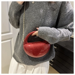 Detail of red glitter acrylic half-moon bag with gold chain strap on a model
