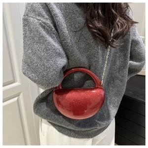 Detail of red glitter semi-circle evening bag with gold chain strap on grey sweater