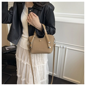 Detail of khaki woven bucket bag with drawstring and metal closure on a stylish model