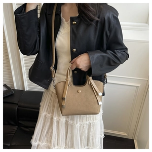 Close-up of khaki woven leather handbag with metal accents on a shoulder strap