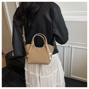 Detail of khaki woven bucket bag with leather strap shown in a minimalist studio setting