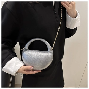 Close-up of silver glitter acrylic crescent bag with golden chain strap on a black outfit