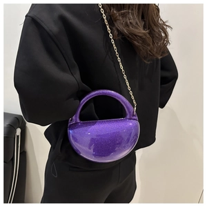Detail of purple glitter dome evening bag with gold chain strap on a model's shoulder