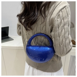 Blue sequin crescent bag with gold chain strap shown on model in minimalist room