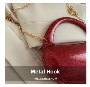 Detail of gold metal hook and chain strap on red glitter acrylic evening clutch bag