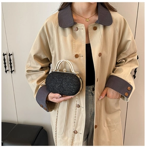 Dettaglio pochette nera glitterata con manico dorato e catena su un elegante trench coat