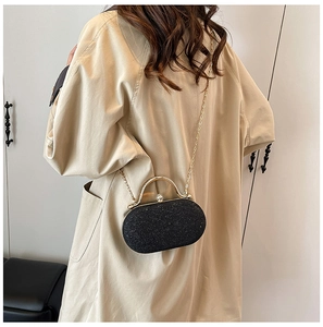 Elegante borsa da sera glitterata nera con cornice dorata e tracolla su una modella