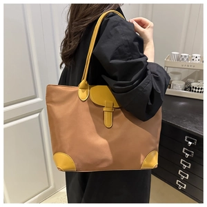 Detailed side view of large brown and yellow tote bag worn by model in a modern room