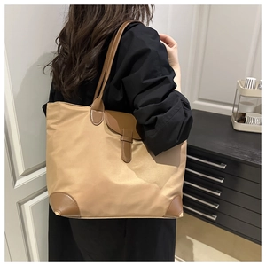 Detail view of khaki large capacity tote bag with brown leather corners on a model