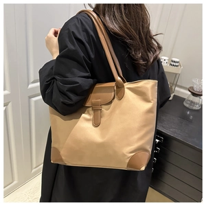 Detail view of khaki nylon tote bag with brown leather trim worn by a model