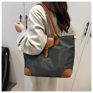 Modern grey nylon tote bag with brown leather accents shown on shoulder in stylish interior