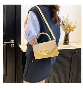 Detail of yellow crossbody bag with gold sequin flap and metallic T-shaped buckle clasp