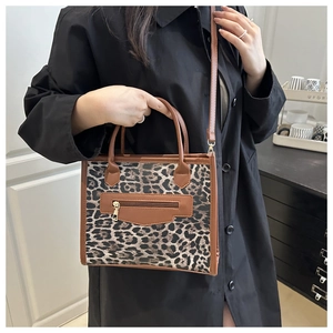 Detail of leopard print tote bag with brown leather trim and adjustable strap worn by model