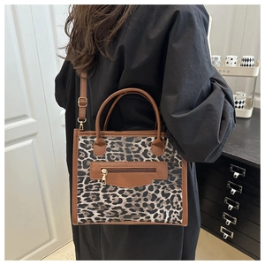 Detail of leopard print crossbody bag with brown leather trim and zipper hardware on model