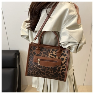 Detail view of leopard print tote bag featuring brown leather trim and side zipper pocket