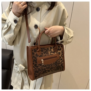 Detail of leopard print tote bag with brown leather trim and metal zipper pocket