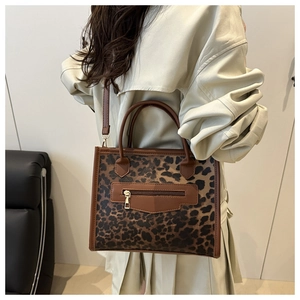 Detail of leopard print tote bag with brown leather straps worn by model in beige coat