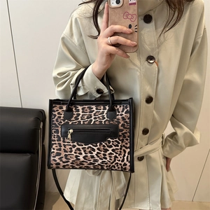 Large leopard print tote bag with black leather straps styled with a khaki trench coat