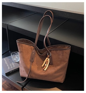 Detail of dark brown suede tote bag featuring natural wood bead tassel and long shoulder strap