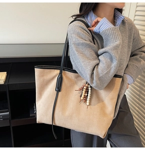 Detail of beige suede tote bag with black straps and vintage beaded tassel ornament