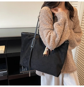 Detail of black suede tote bag with woven beaded charm and slim shoulder straps