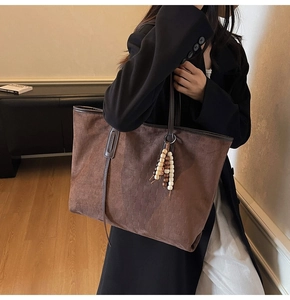 Detail of dark brown suede tote bag featuring a wooden bead pendant and leather handles