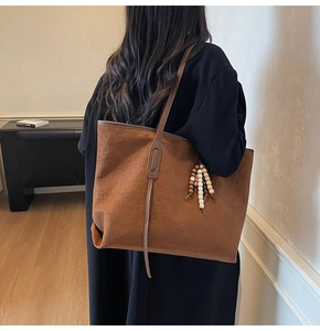 Detail of brown suede tote bag featuring woven texture and wooden bead tassel ornament