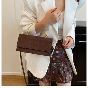 Detail of dark brown quilted handbag with gold ring handles worn with white blazer