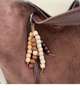 Detail of colorful beaded tassel charm on brown suede tote bag with metallic hardware