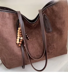 Detail of dark brown suede tote bag featuring wooden bead charm and slim shoulder straps