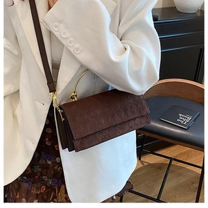 Detail of dark brown quilted handbag with gold handle styled on a white blazer model