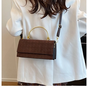 Detail of dark brown quilted suede crossbody bag with elegant gold arc metal handle