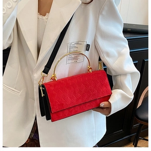 Detail of red quilted crossbody bag with golden metal handle and accordion side design