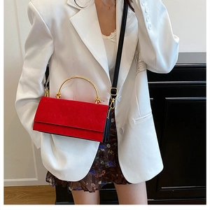 Detail view of red suede crossbody bag with gold metal handle and black shoulder strap