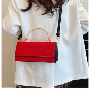 Detailed view of red quilted suede handbag with gold metal handle on a fashion model