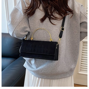 Detail of black quilted crossbody bag with semi-circular gold metal handle and texture