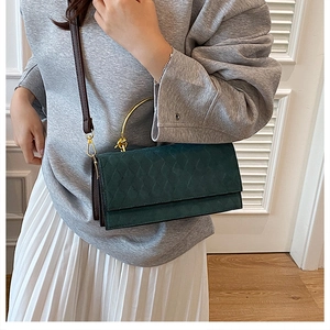 Detail of dark green quilted crossbody bag with a gold circular ring handle and long strap