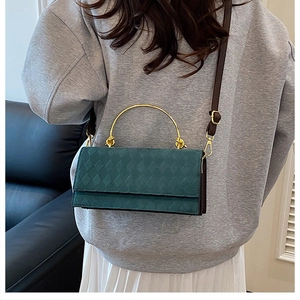 Detail view of dark green quilted handbag featuring gold metal handle and brown strap