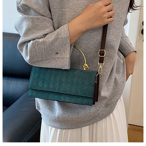 Detail of dark green quilted crossbody bag with golden handle and brown strap