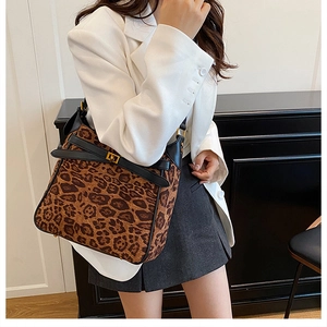 Detail of leopard print crossbody bag with black leather trim and gold buckle on a model
