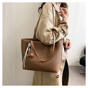 Detail einer braunen Shopper-Tasche mit Lederstruktur, Bärenanhänger und Bandverzierung