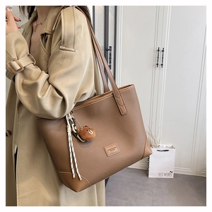 Braune Shopper Tasche aus Leder mit Kieseltextur und Bärenanhänger am Model