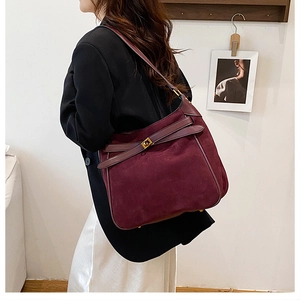 Close-up of wine red suede shoulder bag featuring leather straps and gold metal hardware